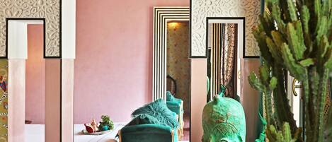 A room with a bed, a green armchair, a cactus sculpture, and a patterned wall.