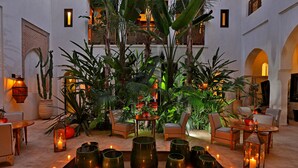 A spacious indoor area with a central seating arrangement surrounded by large planters and candles, creating a warm ambiance. - Dar Kandi (Marrakech)