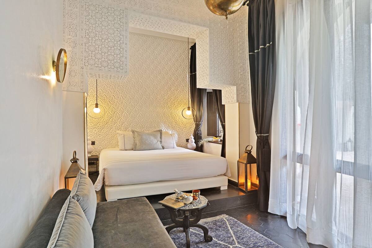Ein modernes Schlafzimmer mit einem großen Bett, einem Schlafsofa, einem kleinen Tisch mit Dekoration und einem gemusterten Teppich.