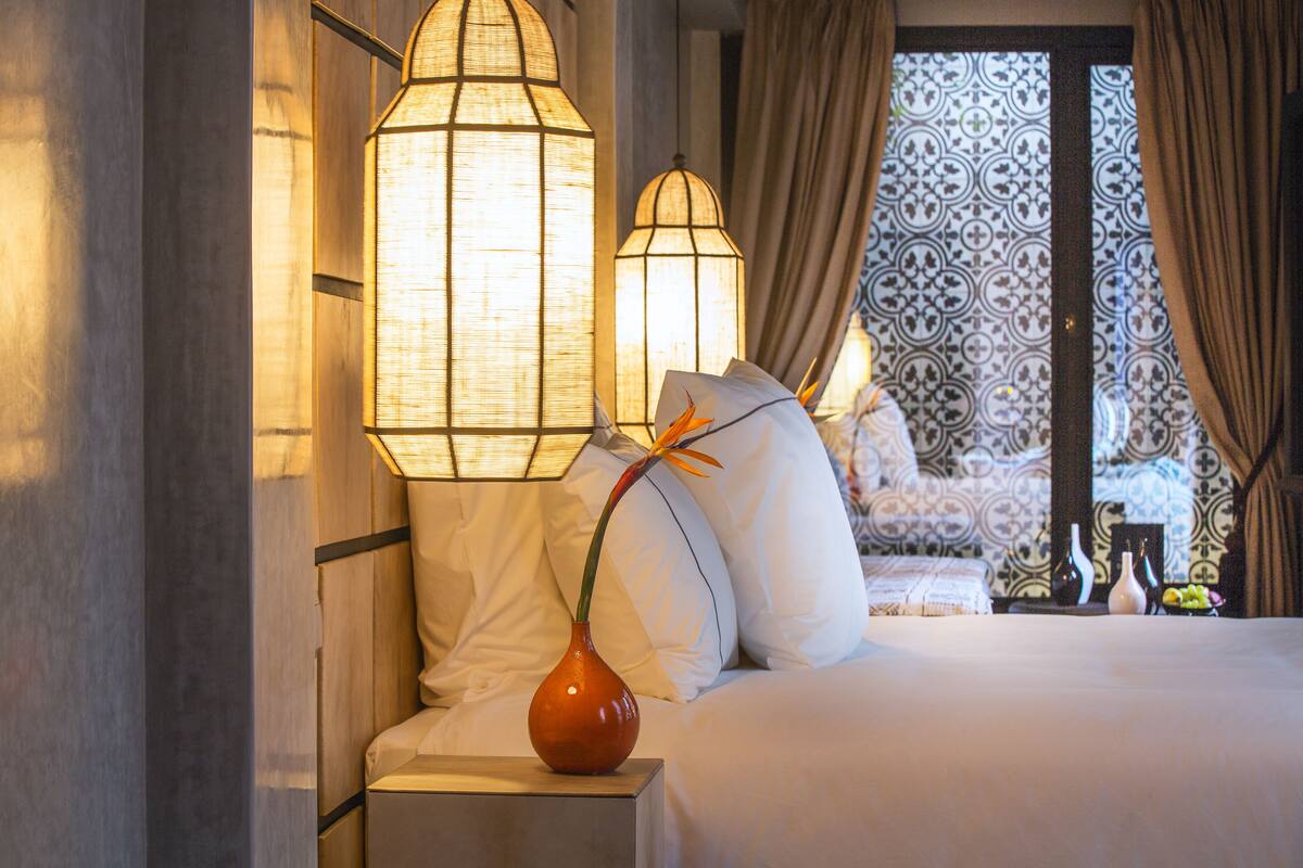Ein Hotelzimmer mit einem Bett, weißen Kissen, einer Vase mit einer Blume und zwei Wandlampen.