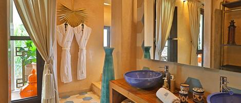 A bathroom with a large mirror, a blue basin, and two towels on a wooden shelf.