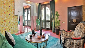 A room with a green sofa, a round coffee table, and a patterned wall. There is a door with a decorative metal gate and a potted plant. - Dar Kandi (Marrakech)