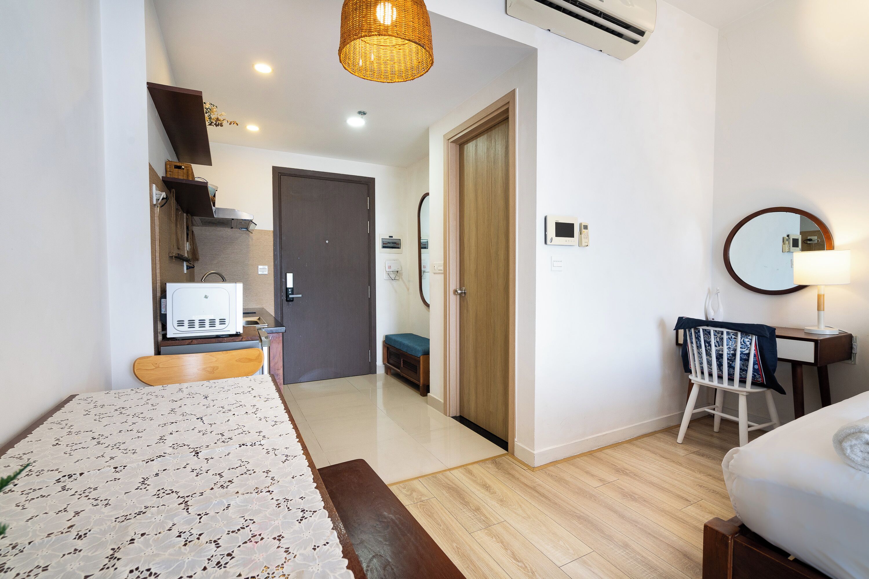 A modern hotel room with a bed, a desk, a chair, a small kitchenette, and a bathroom.