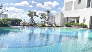 A clear swimming pool with lounge chairs and a modern building in the background. - Saigon Apartment - RiverGate Residence (Ho Chi Minh City)
