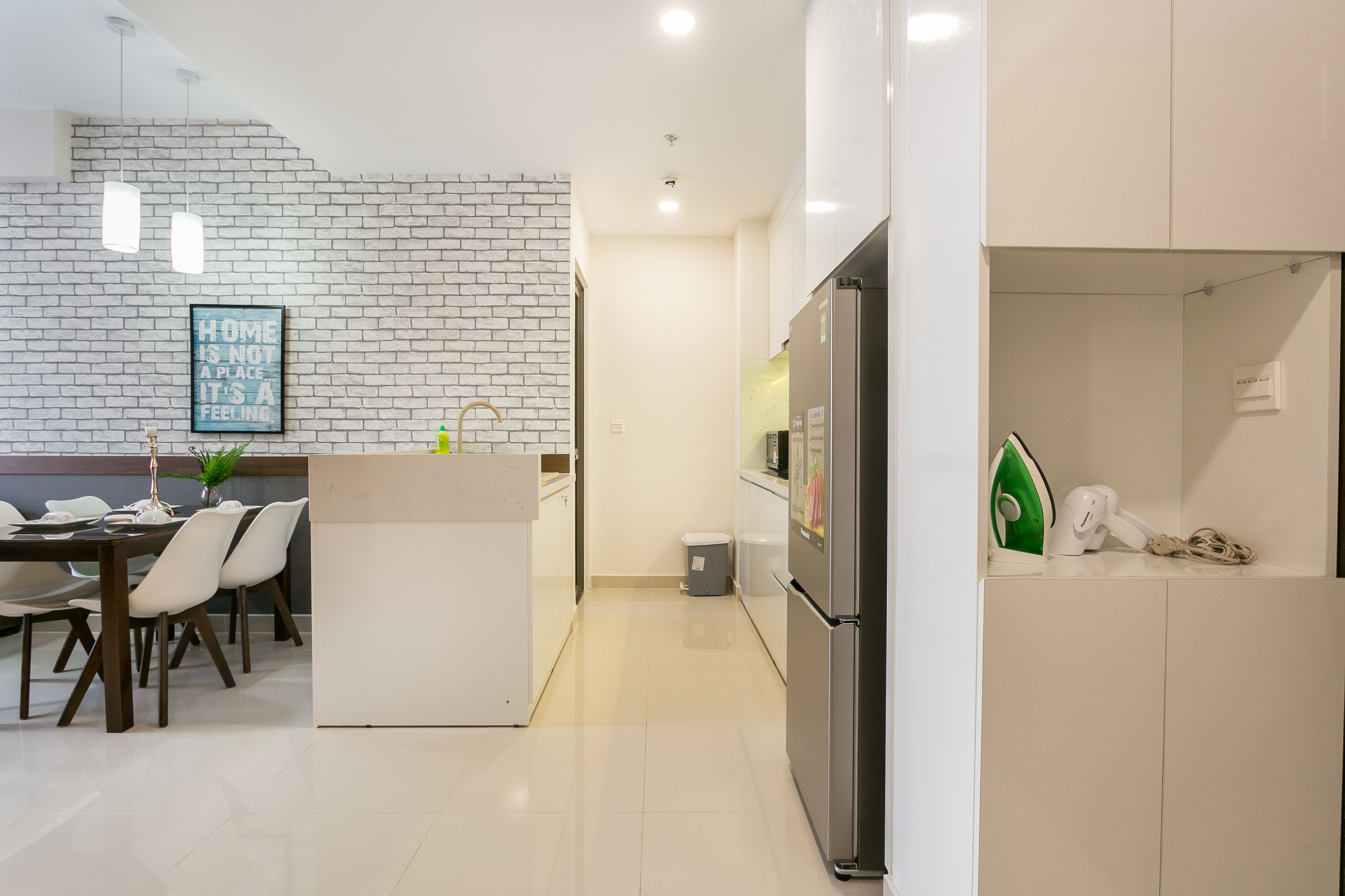 A modern kitchen with a brick wall backsplash, a dining area with chairs, a refrigerator, and an ironing board.