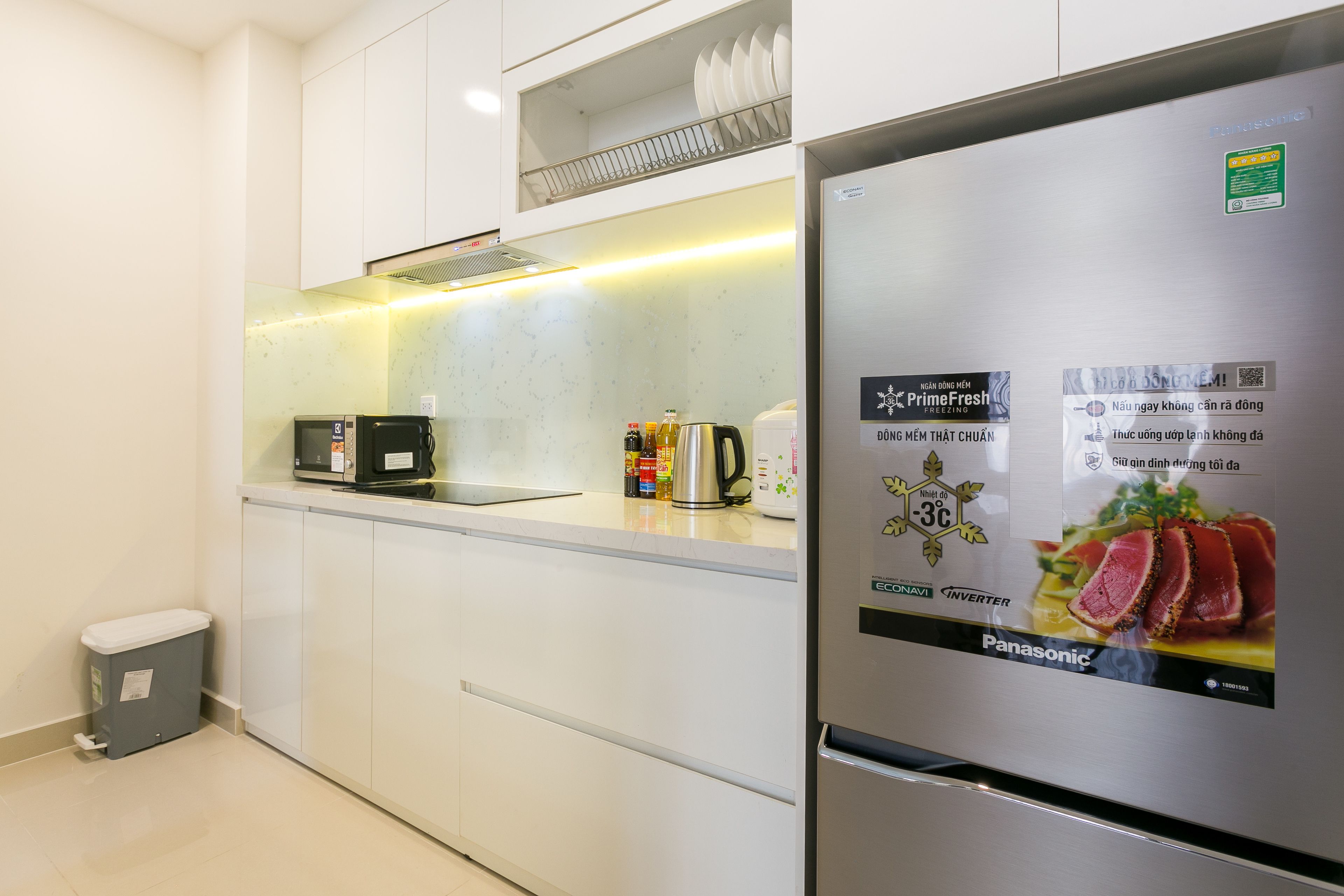 A modern kitchen with white cabinets, a stainless steel refrigerator, a microwave, and a kettle.