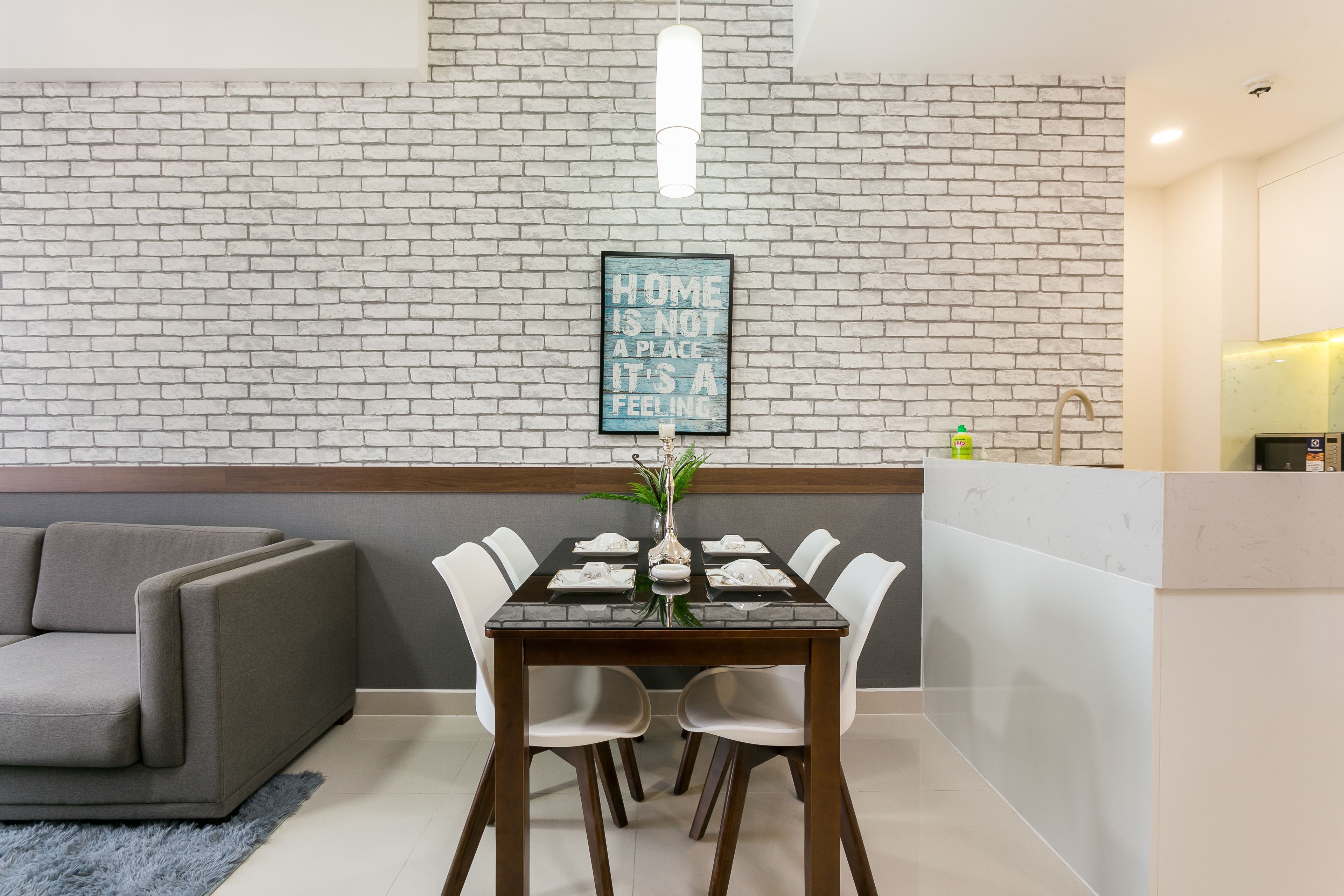 A dining area with a brick wall, a dining table set with white chairs, and a sofa in the background.
