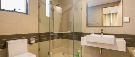 A modern bathroom with a glass-enclosed shower, a toilet, and a sink with a mirror above it.