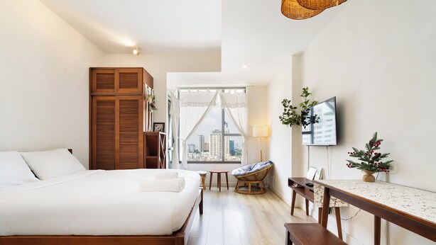 A modern bedroom with a large bed, a wooden wardrobe, a dining table, a chair, a TV, and a city view. - Saigon Apartment - RiverGate Residence (Ho Chi Minh City)
