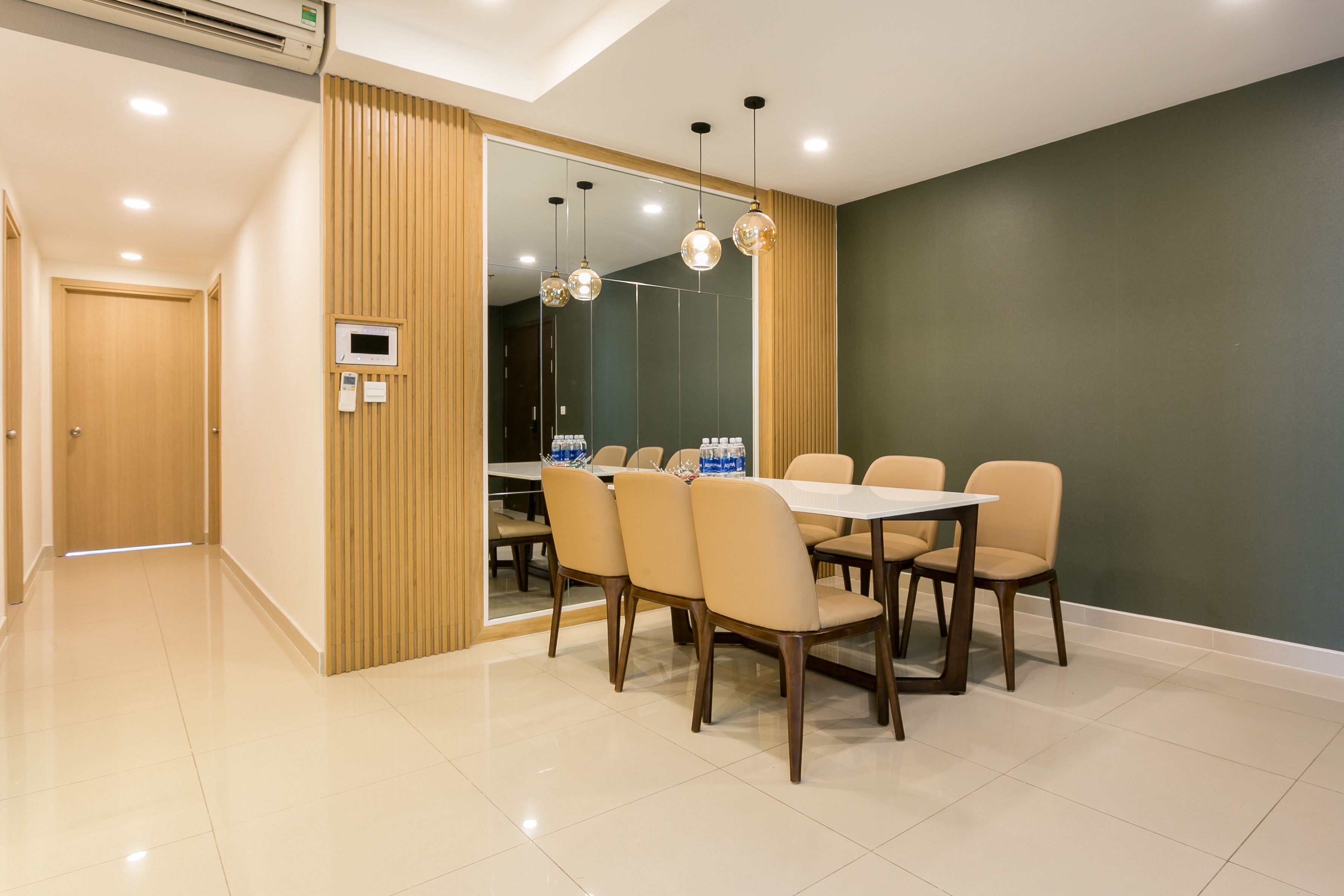 A modern dining area with a large table and chairs, a wooden partition, and a mirror reflecting the room.