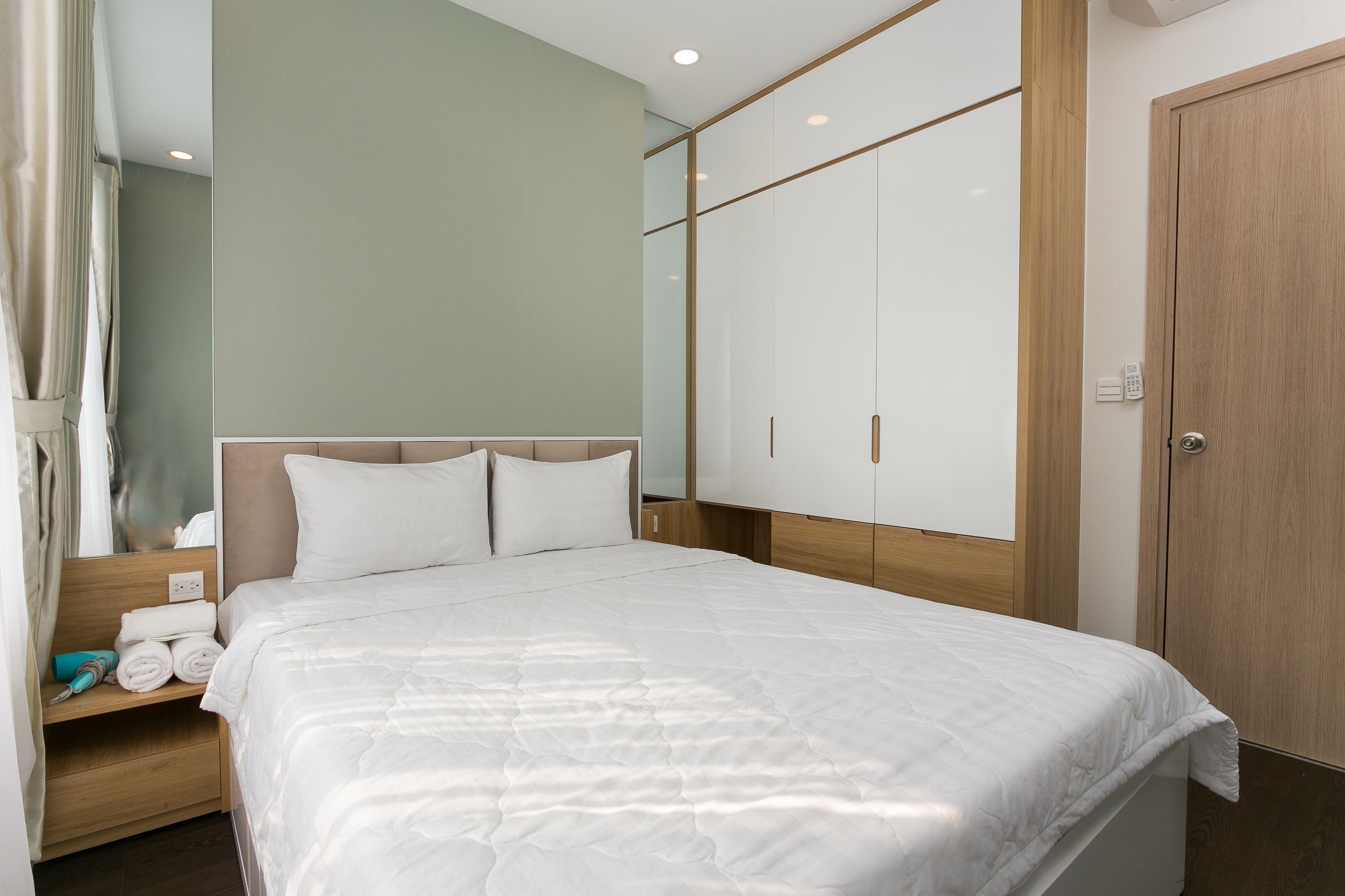 A neatly made bed with a headboard, a wooden wardrobe, and a mirror on the wall.