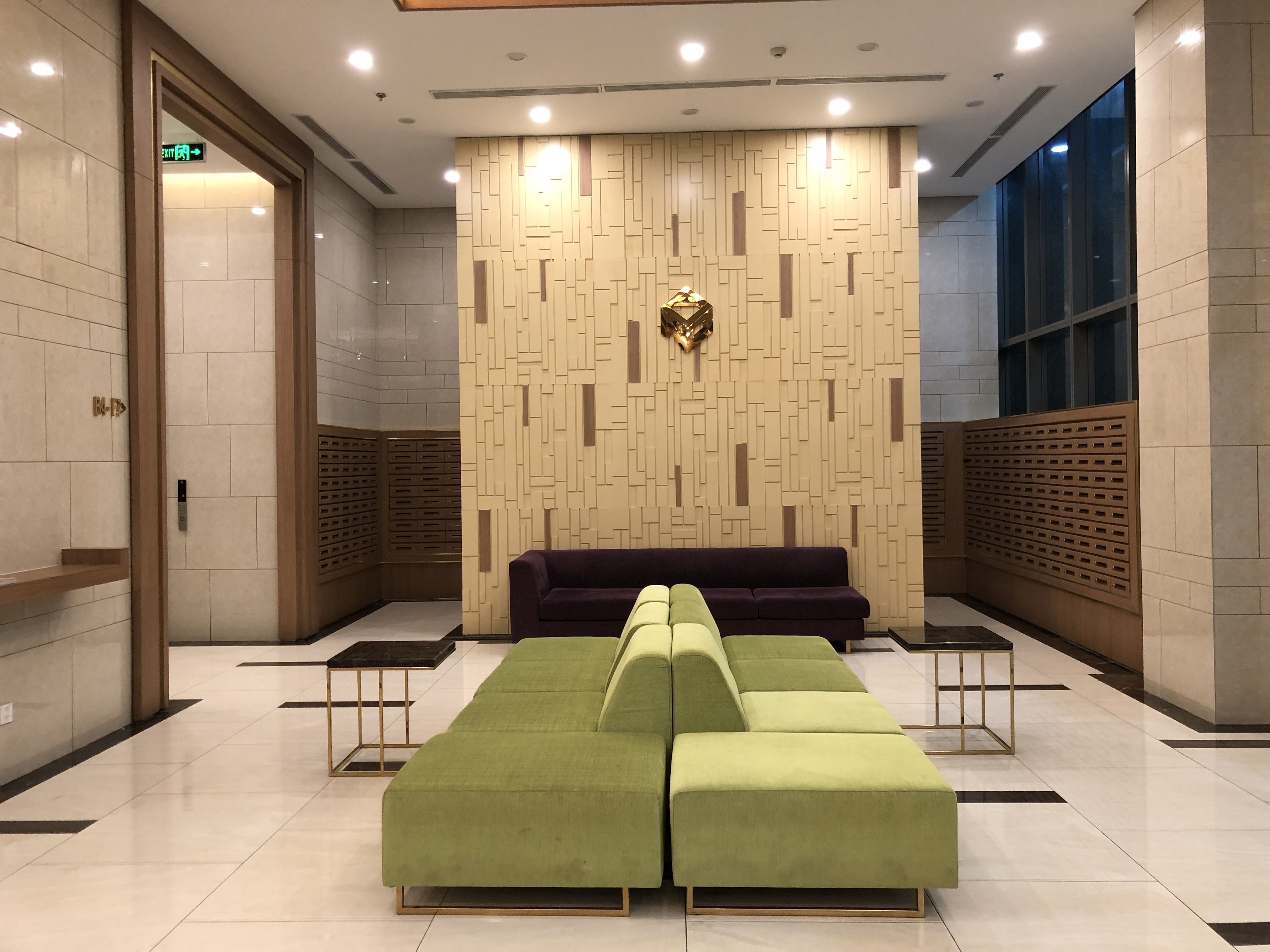 Un hall d’entrée moderne avec un canapé d’angle vert, un canapé violet et un élément décoratif doré accroché au mur.