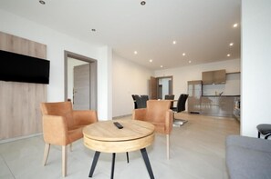 A modern living room with a round wooden table, two leather armchairs, and a grey sofa. A flat-screen TV is mounted on the wall. - Familienhotel Steindl (Millstatt)