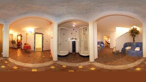 A hotel lobby with a reception desk, a seating area with a blue mosaic sofa, a massage chair, and a shower area with a glass enclosure. - Familienhotel Steindl (Millstatt)