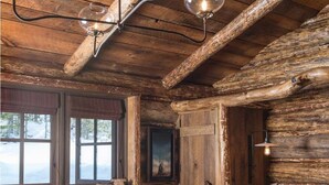 A rustic cabin interior with a wooden log wall, a bed with a fur throw, and a fireplace with logs. - Fish Creek House Bed & Breakfast (Whitehall)
