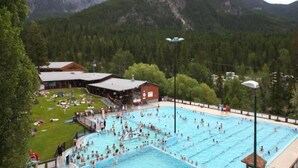 A large outdoor swimming pool surrounded by a building with a roof, set against a mountainous backdrop. - Fish Creek House Bed & Breakfast (Whitehall)