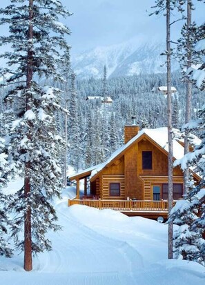 Una cabaña de madera rodeada de árboles nevados y montañas.