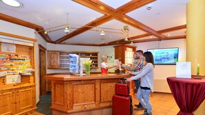 Un espace d’accueil avec un comptoir en bois, une valise rouge et un téléviseur diffusant un paysage.