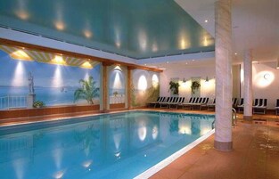 Una piscina al coperto con un murale raffigurante una spiaggia, sedie a sdraio e pavimento piastrellato.