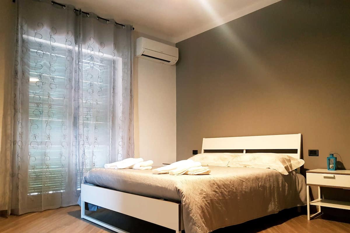 Une chambre à coucher comprenant un lit, une table de chevet, une fenêtre avec des rideaux et un appareil de climatisation.