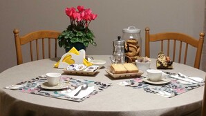 A round table with a floral tablecloth, a world map on the wall, a potted plant with pink flowers, a coffee maker, cookies, and a small figurine. - B&B Tre Passi Dalla Torre (Montesarchio)