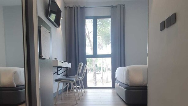 A modern hotel room with a wooden floor, a desk with chairs, a bed, and a large window with curtains. - H La Cabaña (Pozuelo de Alarcon)