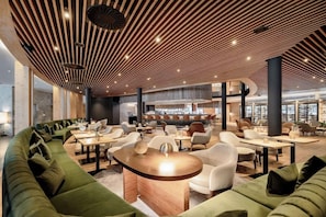 A modern lounge area with a curved green sofa, round tables, and a wooden ceiling with slatted design. - Aqua Dome Therme (Laengenfeld)