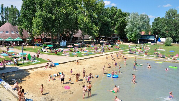 A beach with people swimming and sunbathing, umbrellas, and a grassy area with chairs. - Happy Camp mobile homes in Füred Camping (Balatonfured)