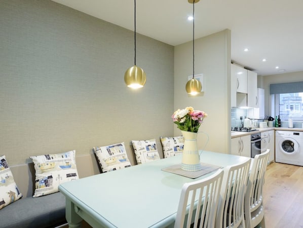 A modern kitchen with white cabinets, a washing machine, and a dining area with a table and chairs. - Sandpipers Loft (North Berwick)