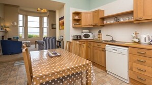 A compact kitchen with wooden cabinets, a white dishwasher, and a dining table with a polka dot tablecloth. - Tensea -charming 3-bed Apartment in North Berwick (North Berwick)