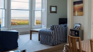 A room with large windows, a striped sofa, a small table, and a bookshelf. - Tensea -charming 3-bed Apartment in North Berwick (North Berwick)