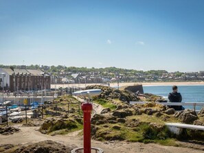 A coastal view with a rocky foreground, a red fire hydrant, and a person sitting on a bench overlooking the sea.