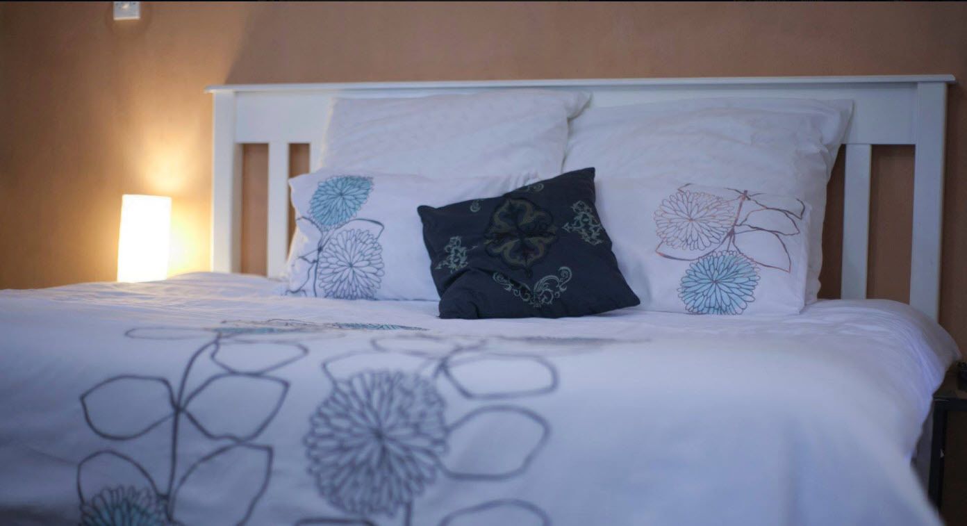 A bed with a white headboard, a floral-patterned bedspread, and two pillows with a leaf design.