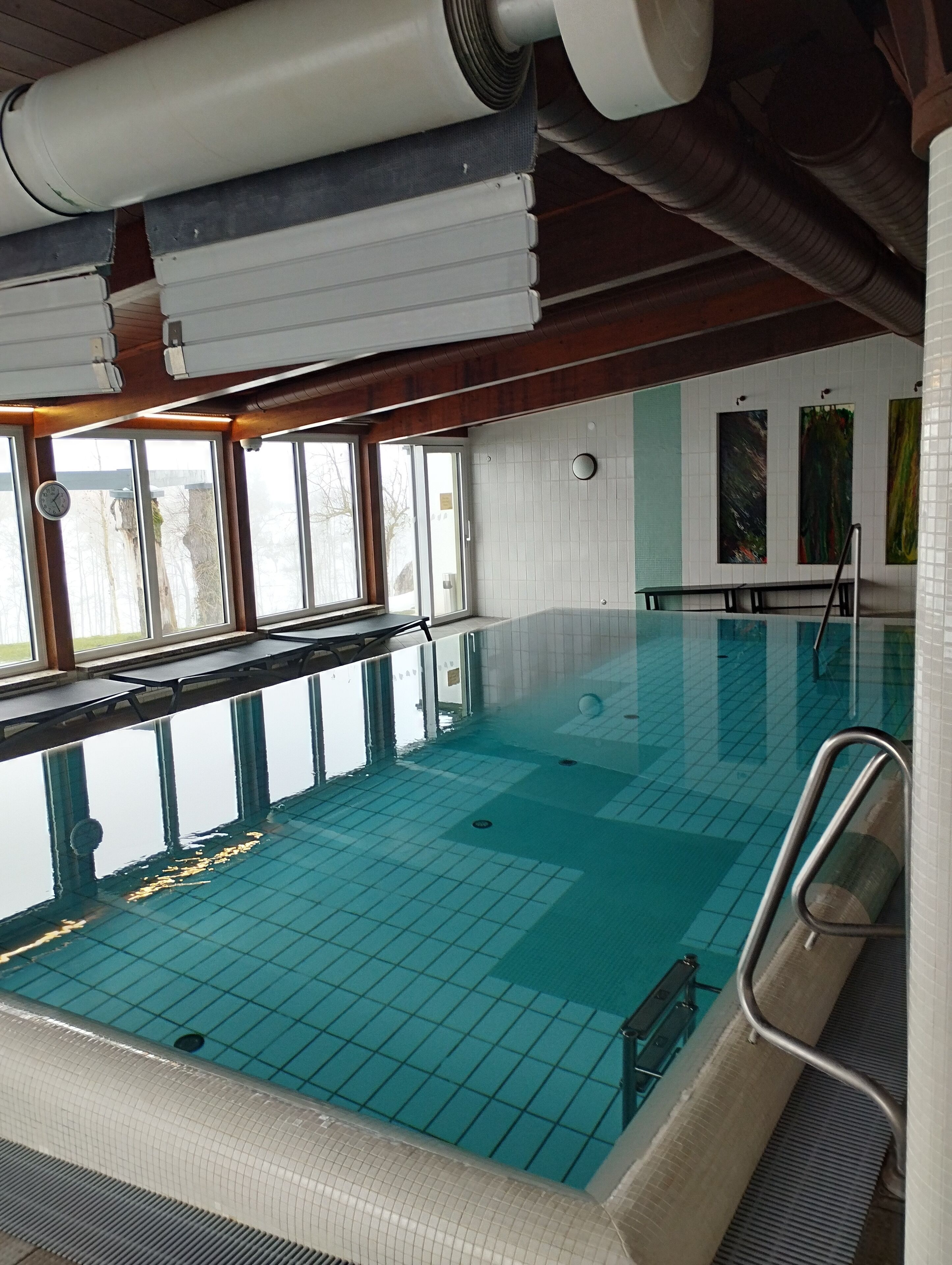 En inomhuspool med kristallklart blått vatten, ett kaklat golv och en vägg med fönster.
