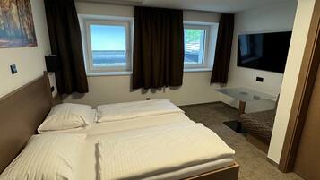 A hotel room with a large bed, two windows, a flat-screen TV, and a small desk area.