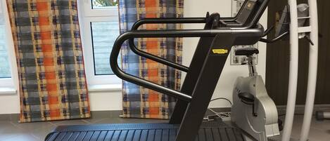 A treadmill in a room with a window, curtains, and a wall-mounted air vent.