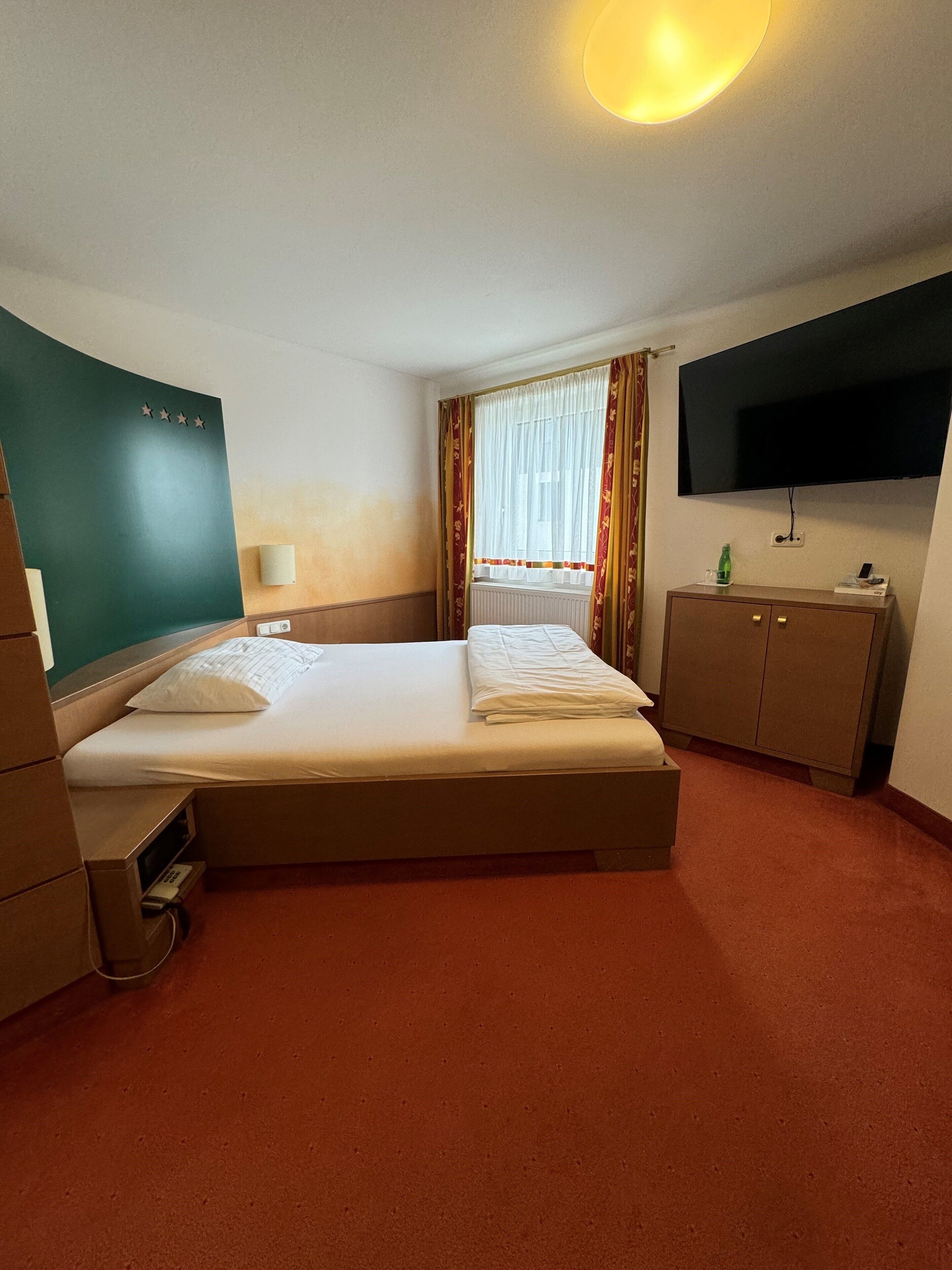 Une chambre d’hôtel avec un lit, une télévision, un bureau et une fenêtre avec des rideaux.