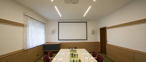A conference room with a long table, chairs, a projector, and a screen.