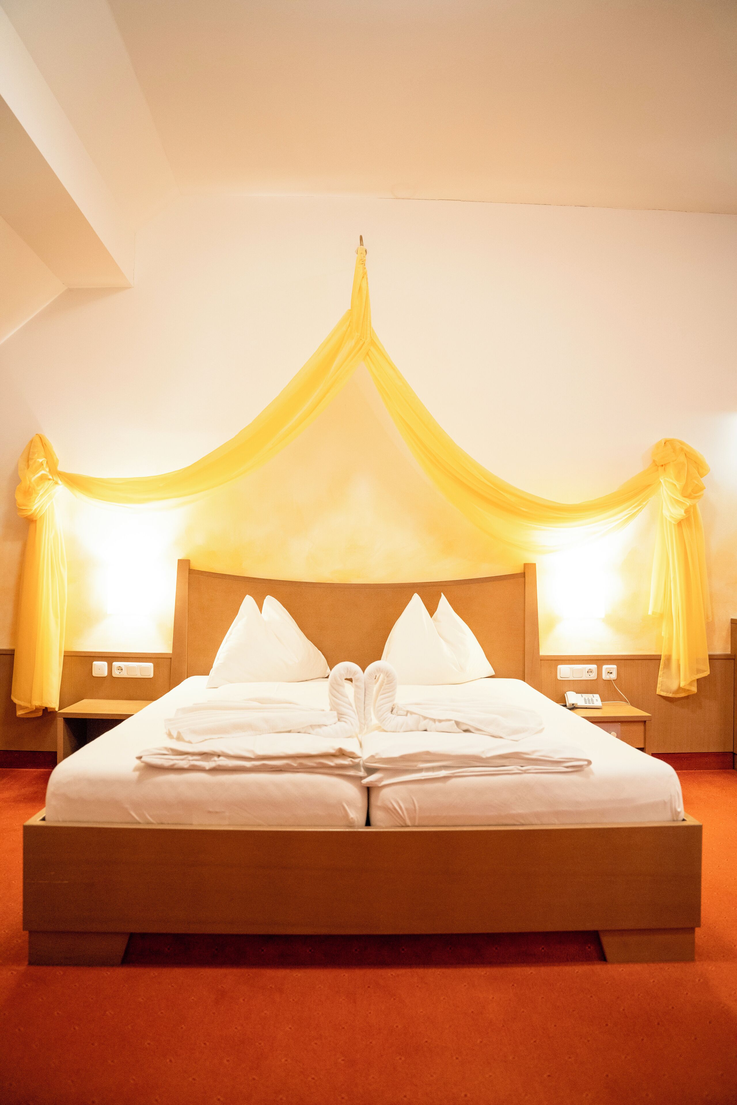 A large bed with a canopy, two bedside tables, and a nightstand with a lamp.
