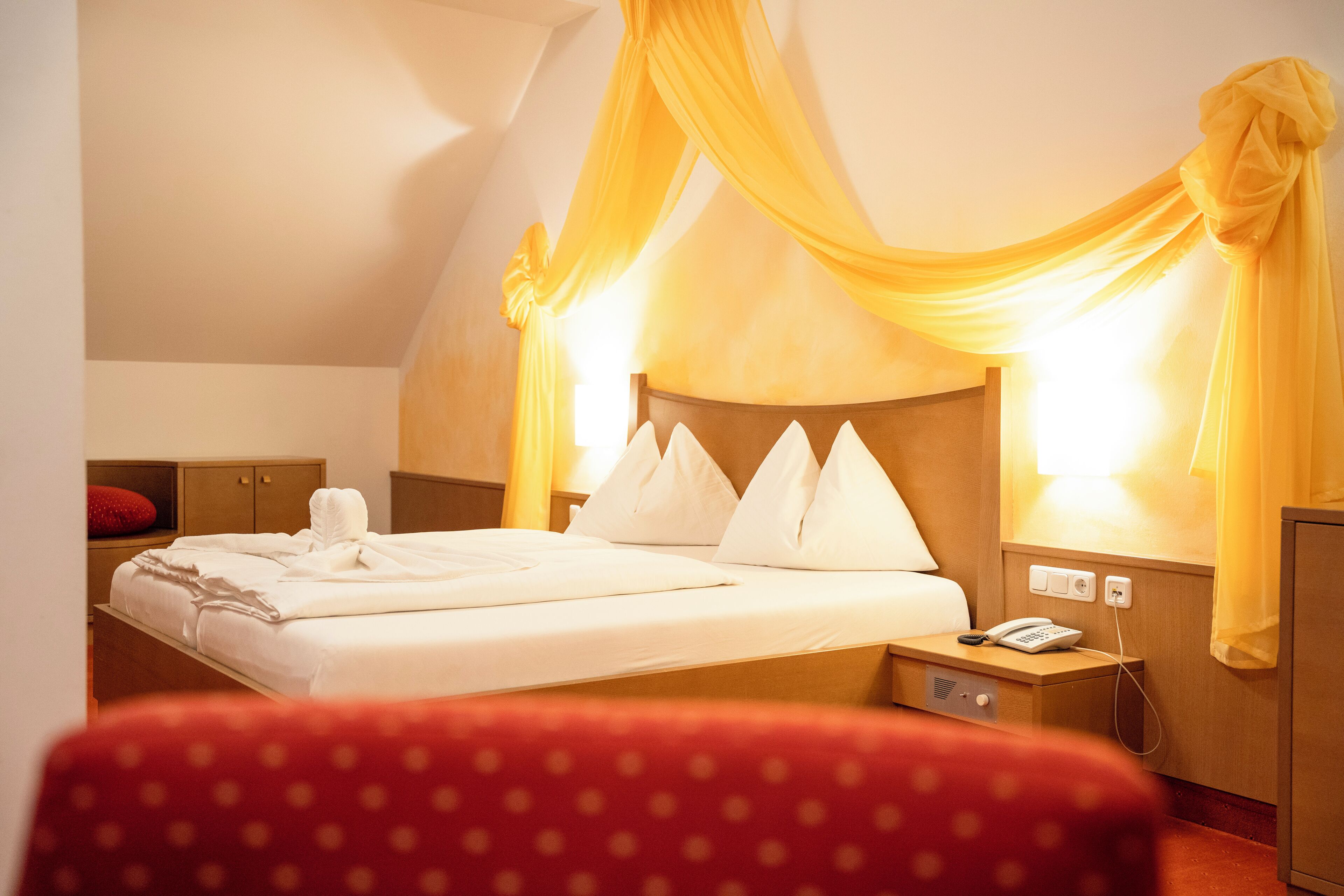 Una habitación de hotel con cama, mesita de noche, teléfono y una silla roja.