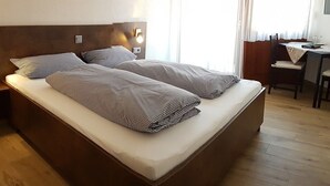A double bed with a headboard, bedside lamps, and a desk with a chair.