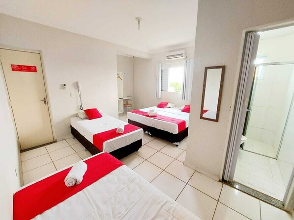 Une chambre d’hôtel avec trois lits, une salle de bain et une porte-fenêtre coulissante donnant sur l’extérieur.