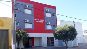 A building with a red and grey facade, labeled "HOTEL JARDIM DO CEDRO," featuring a gated entrance and a small tree in front. - Hotel Jardim Do Cedro (Cedral)