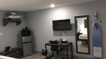 Habitación de hotel compacta con cama, escritorio con silla, televisor, microondas y refrigerador pequeño.