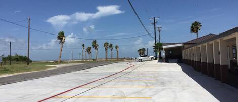 A parking area with marked lanes, a building with a covered walkway, and palm trees in the background.