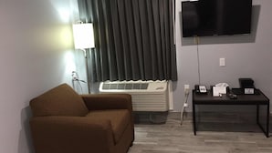 Una habitación con un sofá marrón, un televisor de pantalla plana montado en la pared, un calentador y una mesa con un teléfono y una caja de pañuelos.