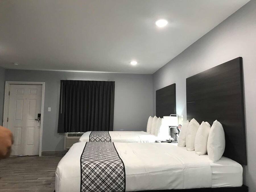 Habitació d'hotel amb dos llits, un mirall gran, una porta i una finestra amb cortines.