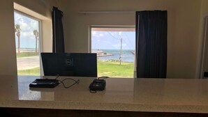 Una habitación con escritorio, computadora y teléfono. Hay ventanas con cortinas, y vista a la playa y al océano.