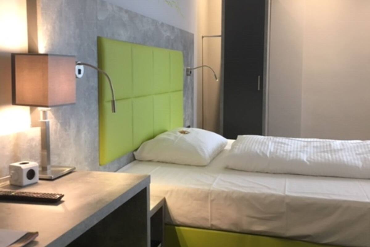 Una habitación de hotel con una cama, un escritorio con lámpara y una pared verde decorativa.