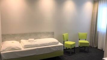 Habitación de hotel con una cama, dos sillones verdes, una ventana con cortinas y piso alfombrado.